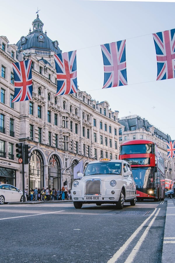 THis is aphoto of the city of London iwht Flags, Red Bus and Taxi driving along the street