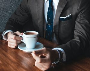 Photograph of man in a grey suit drinking coffee