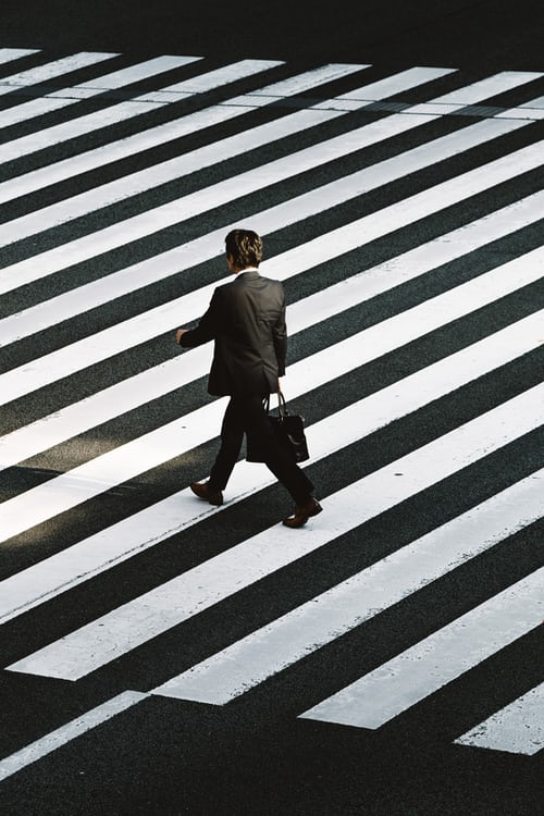 Photo in black and white of man walking on a zebra crossing